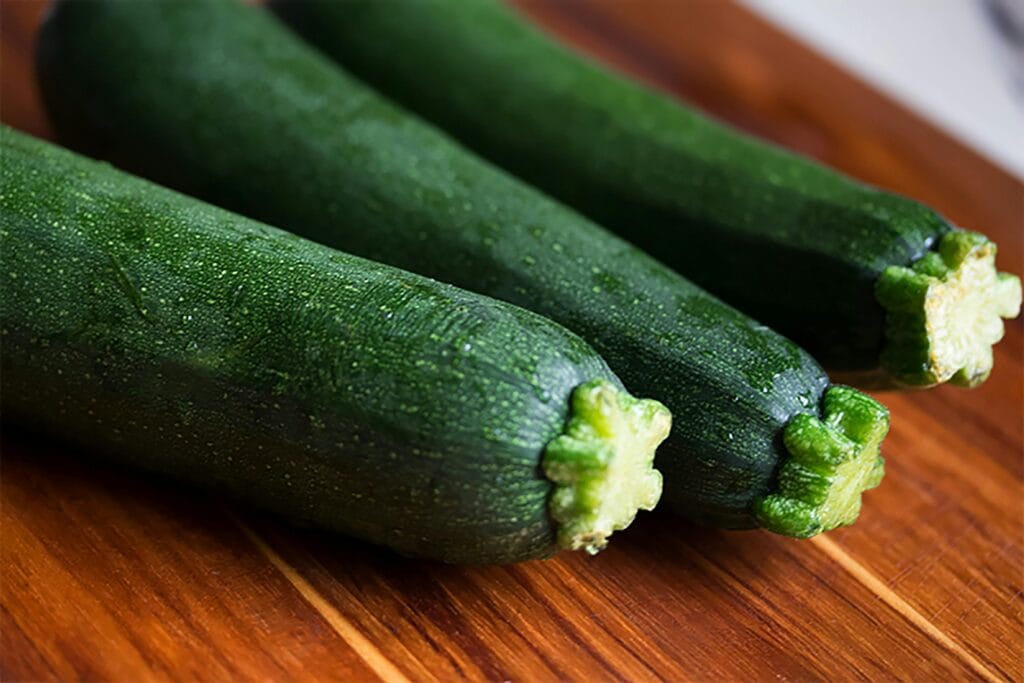 Crispy Air-Fryer Zucchini Fries 2 | eat move healthy Close-up of three fresh green zucchinis on a wooden surface, perfect for food themes.