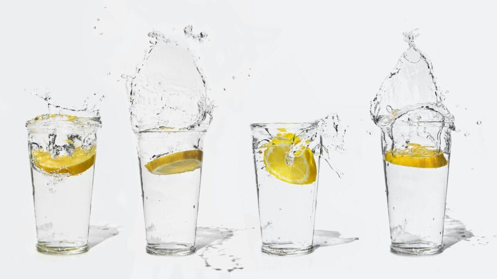 30 Day Fitness Challenge 9 | eat move healthy Four glasses with lemon slices creating splashes of water on a white background.