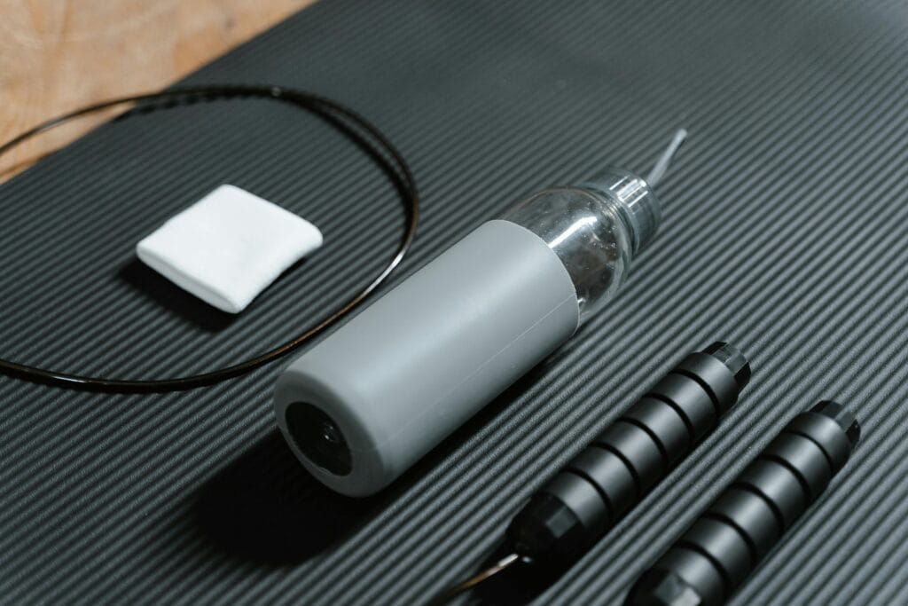 30 Day Fitness Challenge 7 | eat move healthy Gray water bottle and jump rope on textured black yoga mat. Indoor workout essentials.
