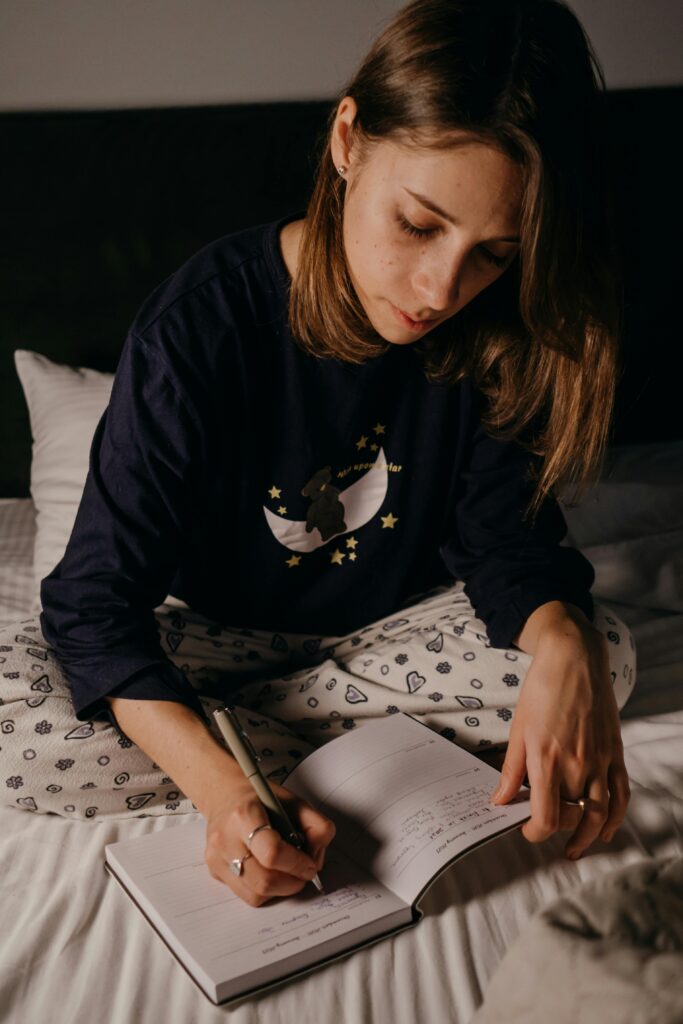 Best Tips to Stop Stress Eating 6 | eat move healthy A young woman writing in a journal while sitting on her bed, captured in an intimate and relaxed atmosphere.