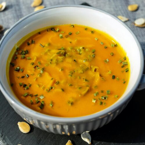 Warm and creamy pumpkin soup garnished with fresh herbs, perfect for a cozy meal.