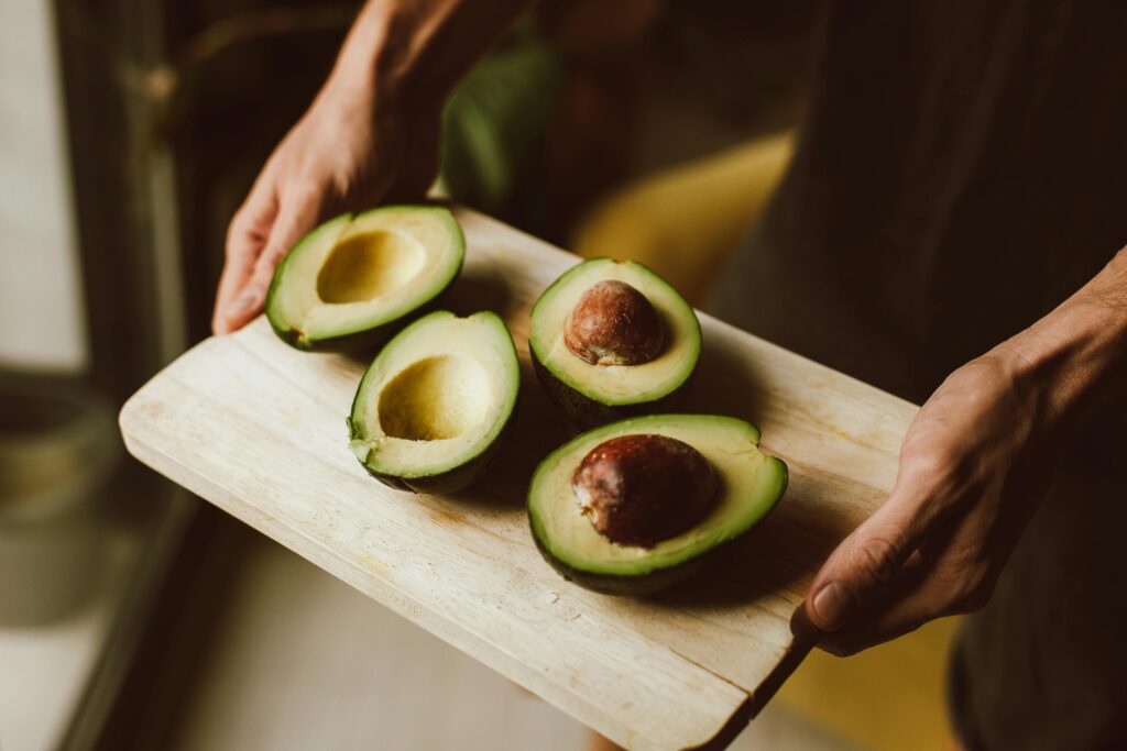 5 Steps Efficient Healthy Meal Planning 7 | eat move healthy A close-up of fresh sliced avocados on a wooden board held by hands, showcasing healthy organic food.