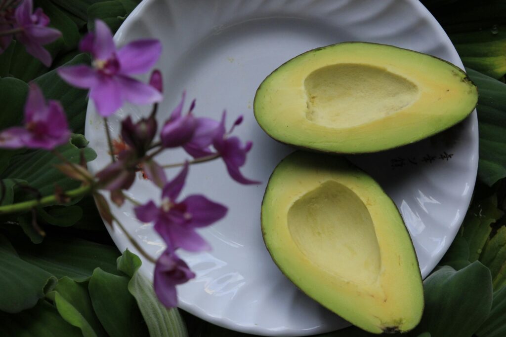10 Foods That Help Burn Belly Fat Naturally 2 | eat move healthy Fresh sliced avocado on white dish with vibrant purple orchids.