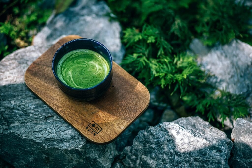 Top view of a green matcha tea served on a wooden tray outdoors, surrounded by rocks.