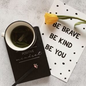 Top view of cup of hot natural tea on notepad placed near tulip on card with wishes